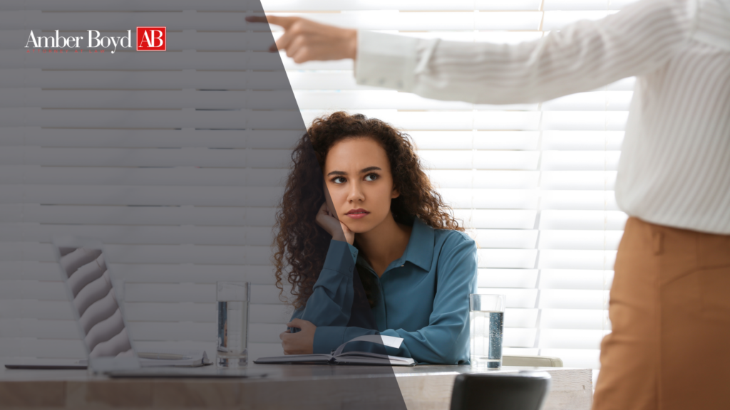 Woman sits at a desk with a notebook, listening thoughtfully during a meeting, with the Amber Boyd AB logo in the top-left overlay.