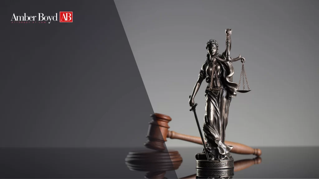 Statue of Lady Justice with scales and sword beside a gavel, against a split dark-gray background with Amber Boyd AB Attorney at Law logo on the left.