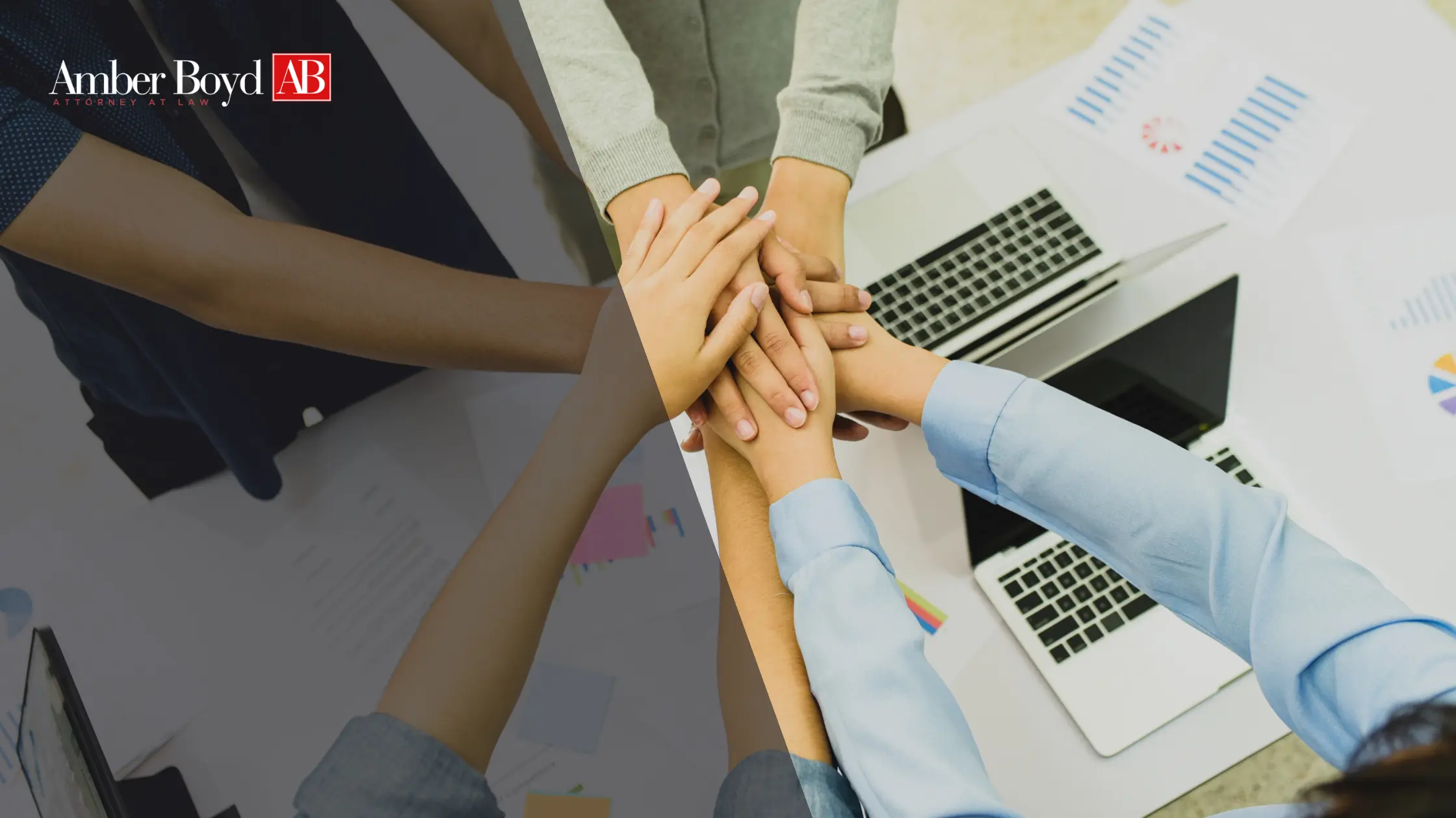 Team members stack hands in the center of a meeting table with laptops, showing collaboration; Amber Boyd logo in the corner.
