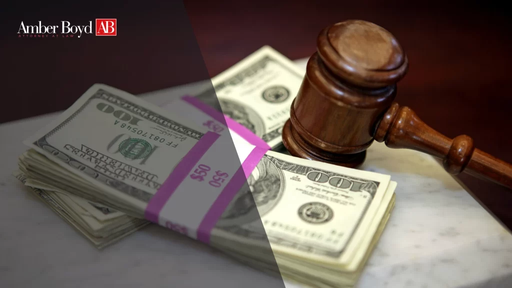 Stacks of U.S. hundred-dollar bills next to a wooden gavel, with an Amber Boyd AB logo in the top left corner.