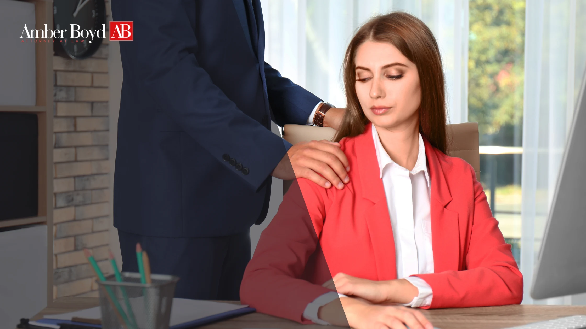 Woman in a red blazer sits at a desk while a man in a navy suit rests his hand on her shoulder; Amber Boyd AB logo in the top-left corner.