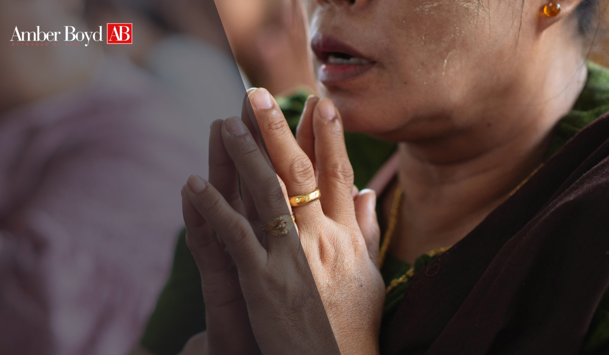 Close-up of hands pressed together in prayer with gold rings, partial face of a woman in background; Amber Boyd logo appears top-left.