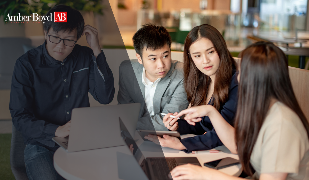 Four professionals gathered around a table in a modern office, looking at a tablet and laptops during a discussion, with Amber Boyd AB logo in the corner.