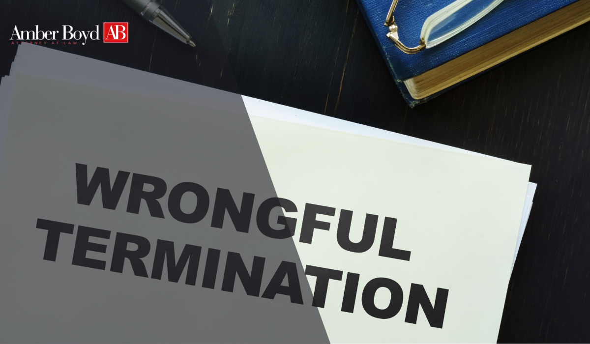 Amber Boyd law logo in the corner with papers reading 'WRONGFUL TERMINATION' on a dark desk beside a blue notebook.