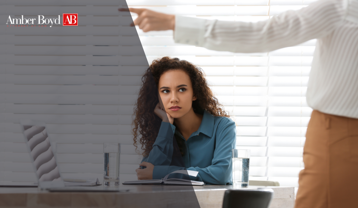 Woman sits at a desk with a notebook, listening thoughtfully during a meeting, with the Amber Boyd AB logo in the top-left overlay.