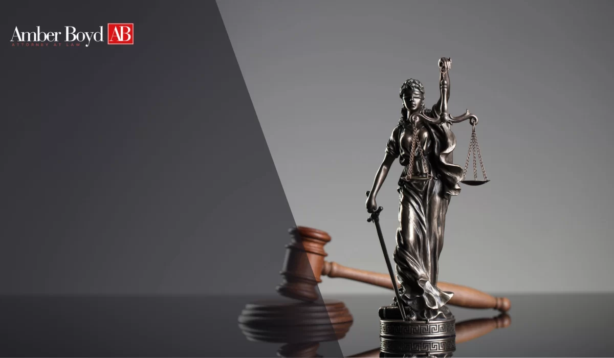 Statue of Lady Justice with scales and sword beside a gavel, against a split dark-gray background with Amber Boyd AB Attorney at Law logo on the left.