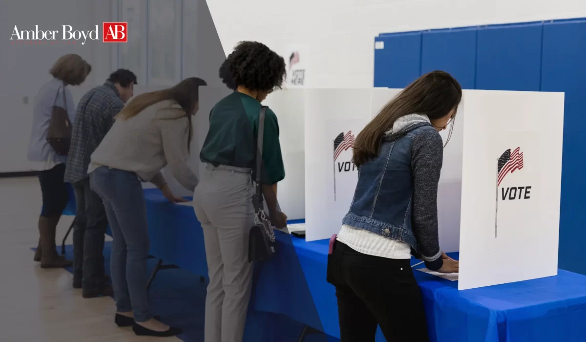 Voters lined up at white voting booths with American flag graphics, in a blue-walled room; Amber Boyd AB logo appears in the top-left corner.