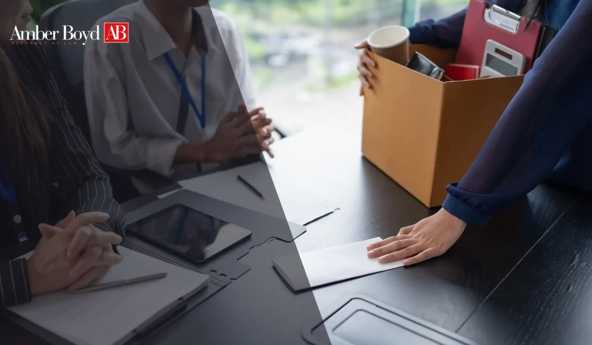 Business meeting at a conference table with a tablet, documents, and a cardboard box of office supplies; Amber Boyd logo in the top-left corner.