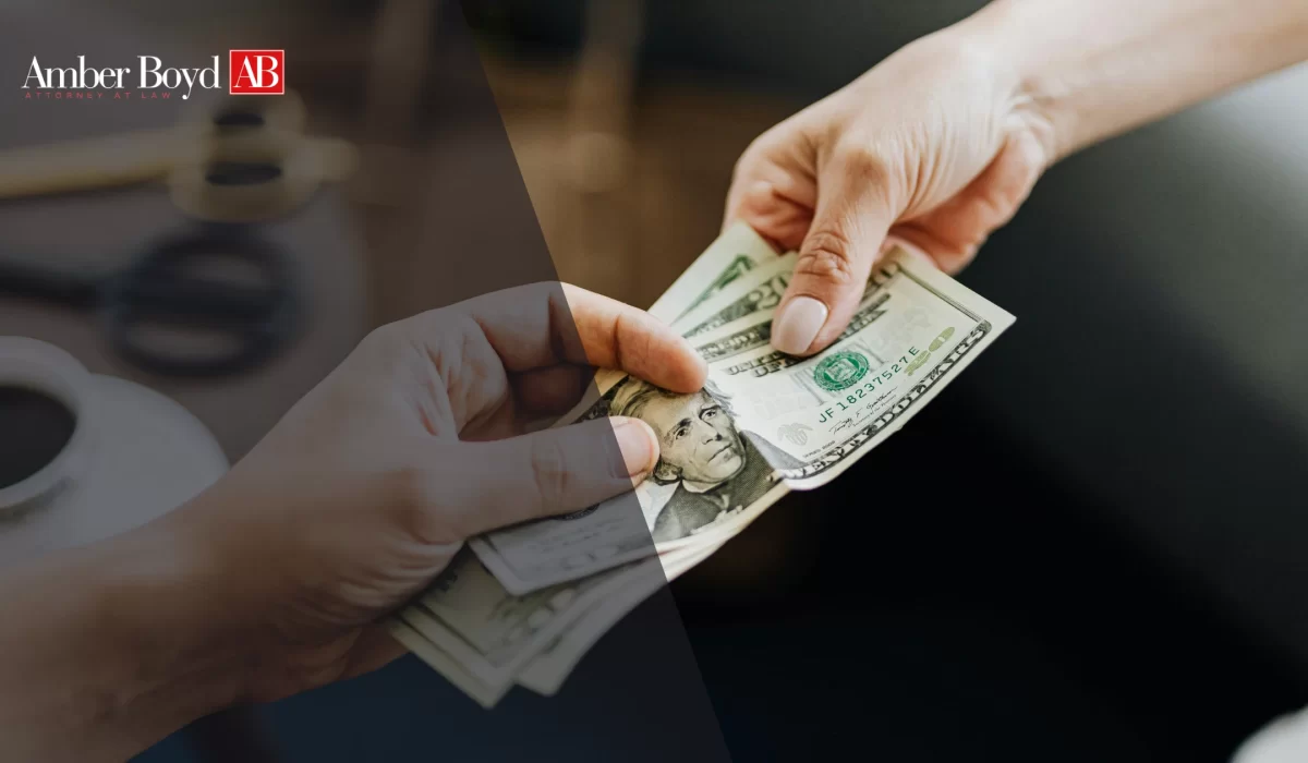 Two hands exchanging a stack of US dollar bills, with a blurred background and Amber Boyd logo in the corner.