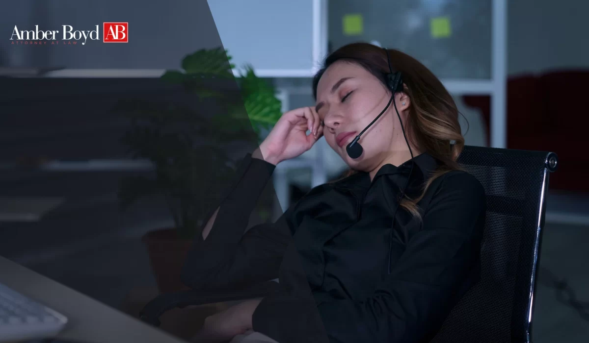 Woman wearing a headset rests her head on her hand at a desk in a darkened office; Amber Boyd AB logo is in the upper left corner.