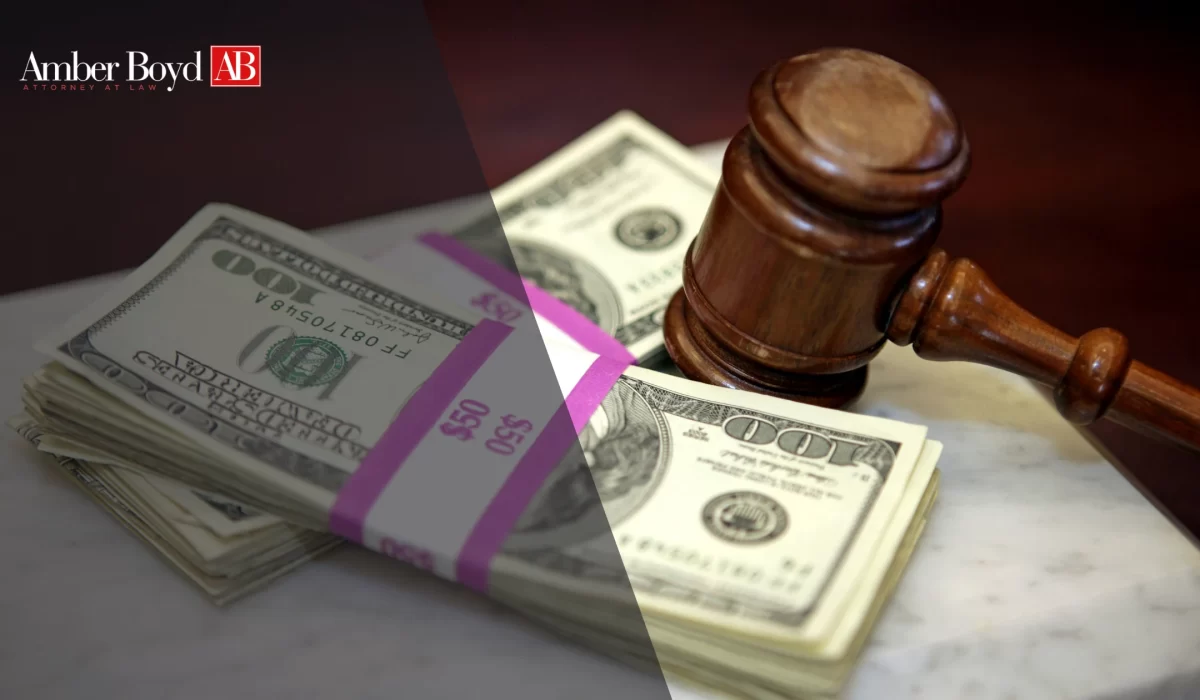 Stacks of U.S. hundred-dollar bills next to a wooden gavel, with an Amber Boyd AB logo in the top left corner.