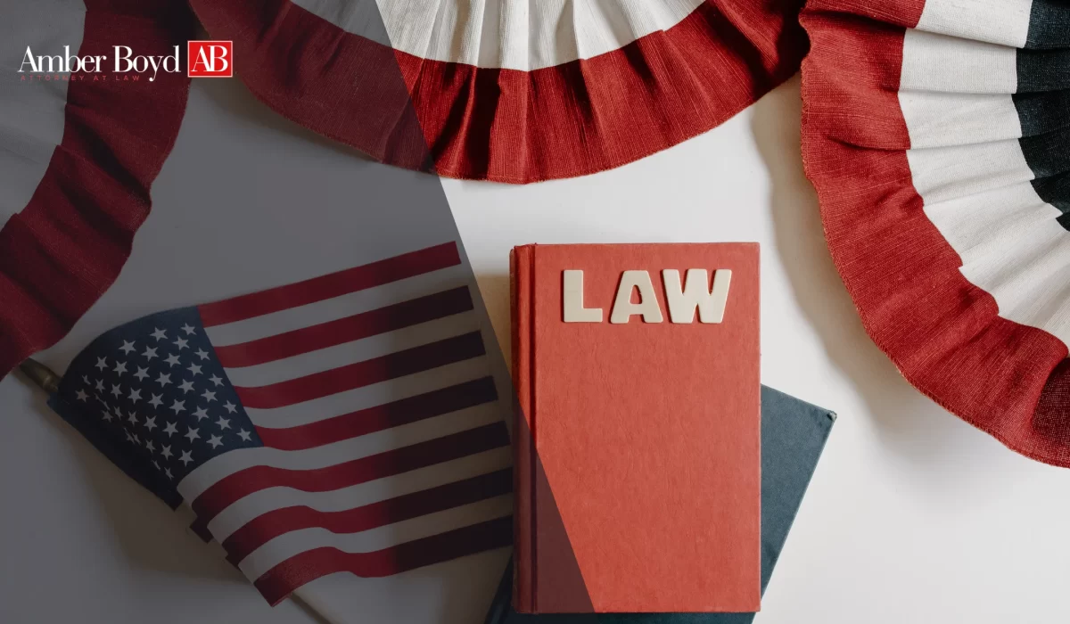 Patriotic law-themed image with a red LAW book, an American flag, and red-white-blue fabric beside the Amber Boyd branding logo in the corner.
