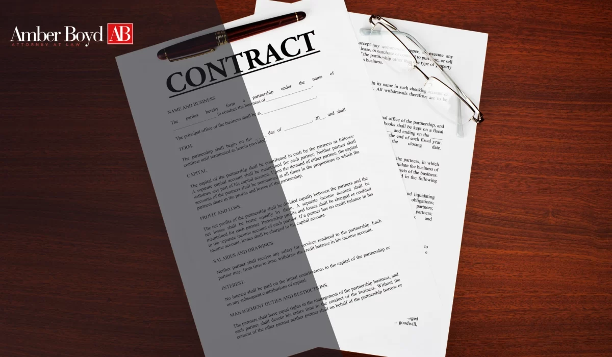 Contract documents on a dark wood desk with a burgundy pen, glasses, and Amber Boyd AB branding in the corner.