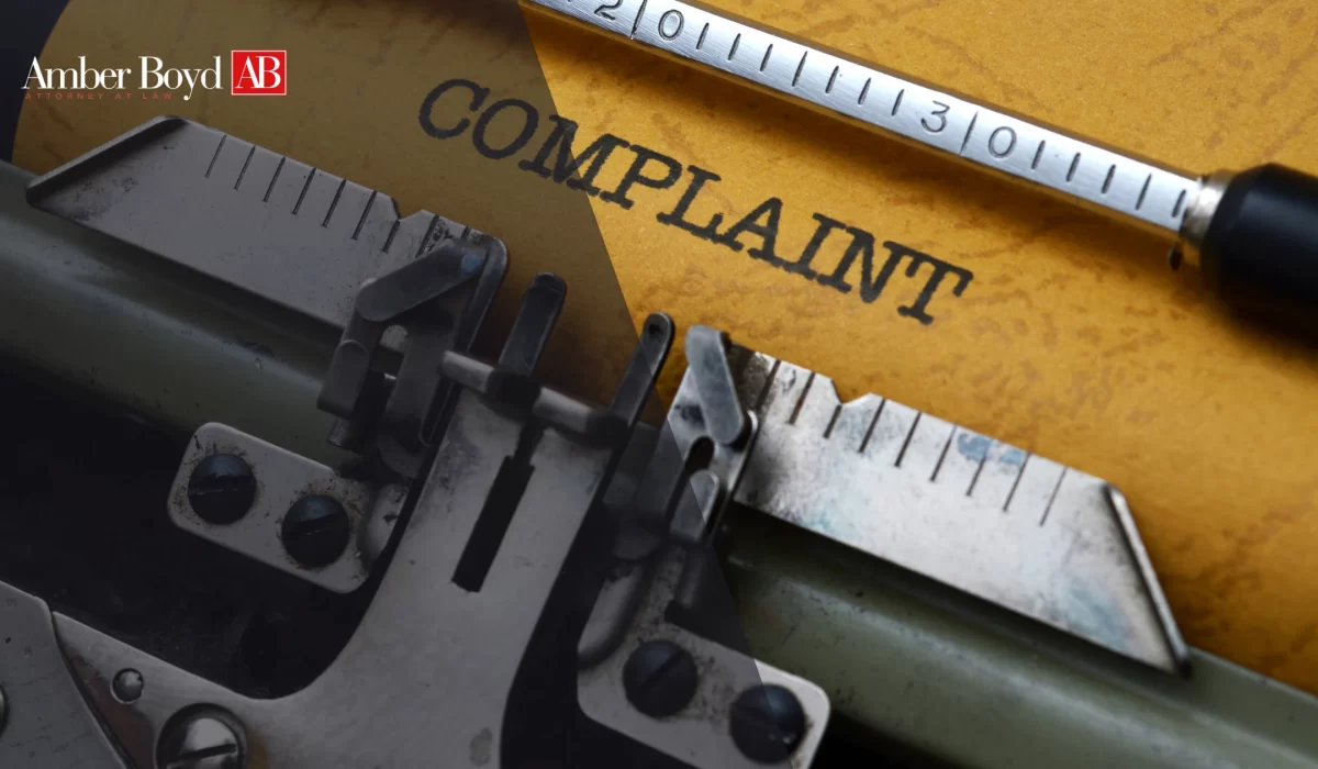 Close-up of a typewriter and ruler on a yellow surface with the word 'COMPLAINT' and the Amber Boyd AB logo in the corner.