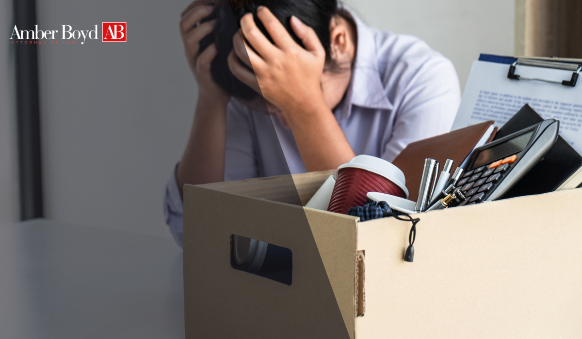 stressed person holding head beside a cardboard box of office supplies, with Amber Boyd Attorneys at Law logo in the corner